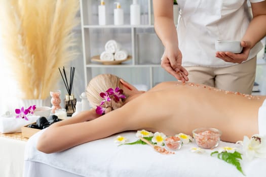 Woman customer having exfoliation treatment in luxury spa salon with warmth candle light ambient. Salt scrub beauty treatment in health spa body scrub. Quiescent