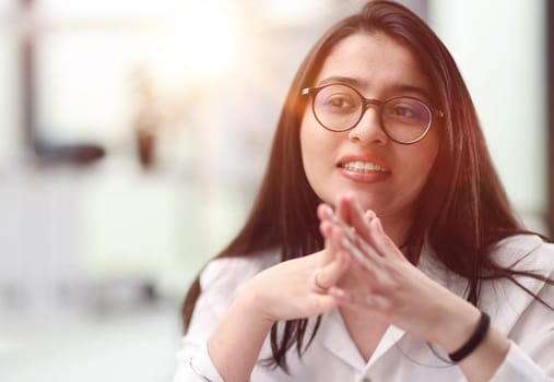 Close-up portrait of a confident and attractive woman in a white blouse and glasses in a classroom or office.