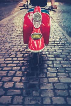 A Man Riding A Scooter Or Moped Down A Cobbled Street In Rome, Italy