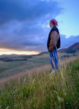 A Girl On A Hillside In Scotland On A Summer's Evening At Sunset, With Focus On Foreground Grass