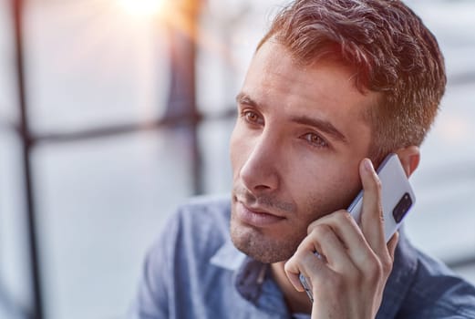 Portrait of young entrepreneur in casual office making phone call while working with laptop