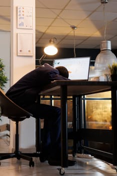 Workaholic drained employee slepping desk in startup office, after checking marketing statistics on computer. Exhausted tired manager working overhours at company strategy plan. Business concept