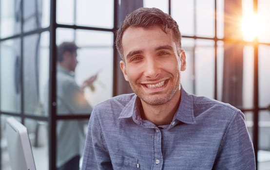 Portrait of young happy businessman wearing and blue shirt standing in his office and smiling with