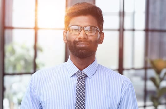 Confident elegant handsome young man standing in the office wearing a blue shirt