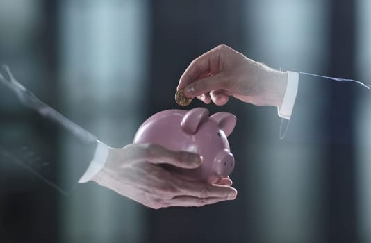 Hand puts a coin in a piggy bank on a black background. accumulation concept