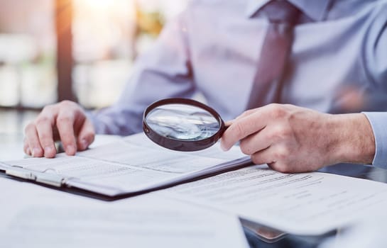 man looking through a magnifying glass to documents notebook.