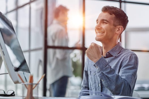 Excited modern businessman sitting at office desk and rejoicing his success