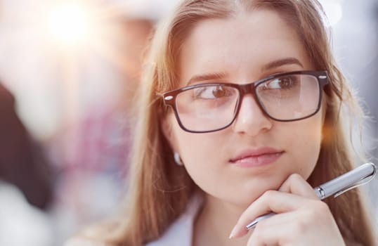 A beautiful young girl in the office works with documents, holds a pen in her hand and looks at the camera.