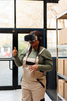 African american employee having fun using virtual reality headset in warehouse, analyzing goods checklist. Storage room supervisor wearing industrial overall, preparing customers orders