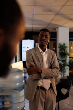 Portrait of african american businessman discussing company profit with coworker during work break in startup office. Employees working late at night, planning investment strategy. Business concept
