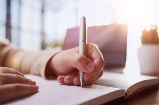 Businessman writes with a pen in diary in a sunny office, business and education concept. Close up