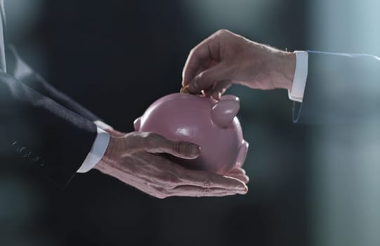 Hand puts a coin in a piggy bank on a black background. accumulation concept