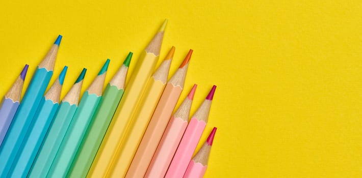Multi-colored wooden pencils on a yellow background, top view. Copy space