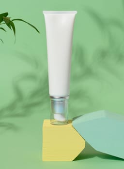 White plastic tube with a transparent cap and dispenser on an green background, container for cosmetics