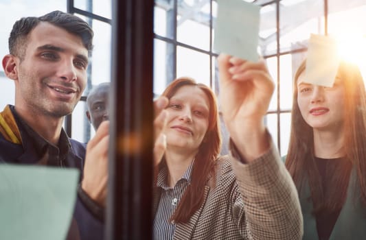 Creative business team looking at sticky notes on glass window