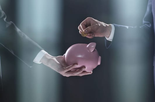 Hand puts a coin in a piggy bank on a black background. accumulation concept