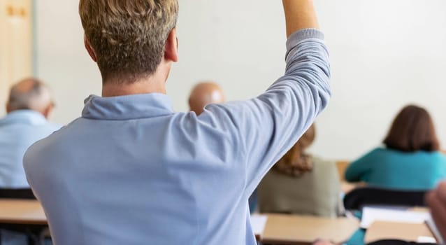 Back view of older student raising his hand to answer teacher's question during education training class. jpg ai image. High quality image