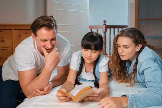 Bedtime story with childhood storytelling, mom and dad reading a fantasy book together to their little young girl in cozy and comfortable bedroom. Modern family happy time. Synchronos