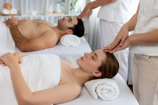 Caucasian couple enjoying relaxing anti-stress head massage and pampering facial beauty skin recreation leisure in dayspa modern light ambient at luxury resort or hotel spa salon. Quiescent