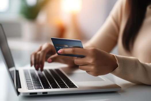 Close-up of female hand holding credit card and laptop making Internet purchase.