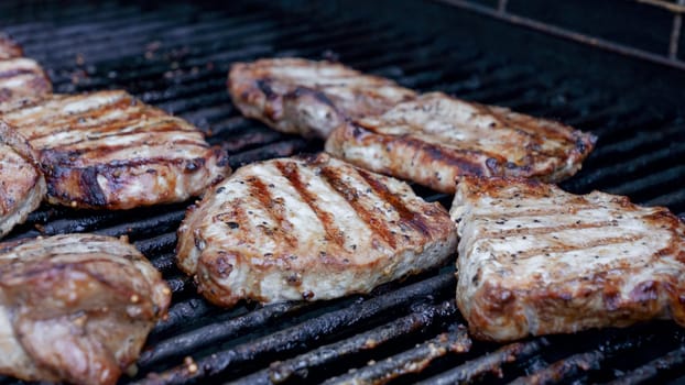 Grilled meat steak on stainless BBQ grill with flames on dark background. Food and cuisine concept