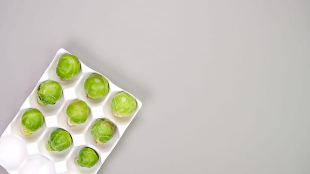 Raw organic Brussel sprouts in yellow white egg container on grey background, top view. Flat lay, overhead, from above. Copy space.