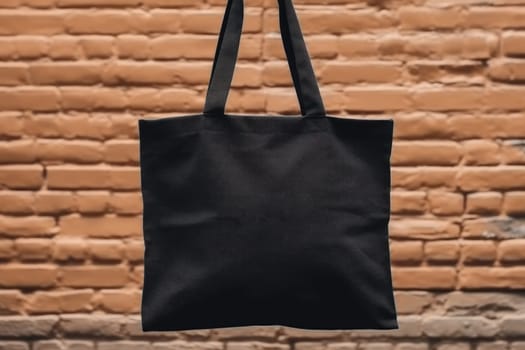 Hand holding black cotton tote bag mockup on a wall background.