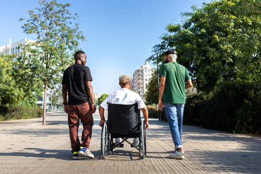 Rear view of young black man in a wheelchair and his male friends walking together in the city. Friendship concept.