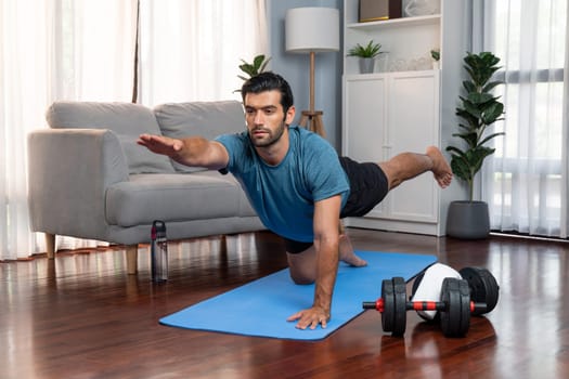 Flexible and dexterity man in sportswear doing yoga position in meditation posture on exercising mat at home. Healthy gaiety home yoga lifestyle with peaceful mind and serenity.
