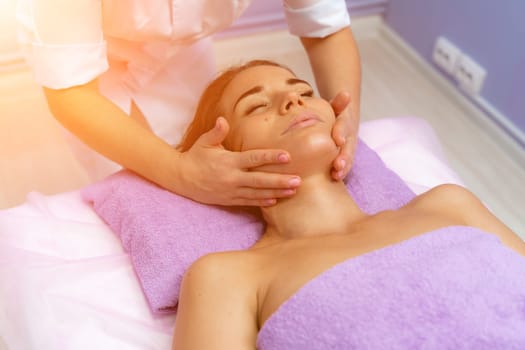 Relaxing massage. European woman getting facial massage in spa salon, side view.