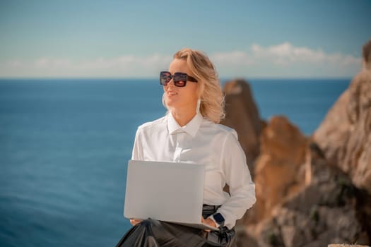 Business woman on nature in white shirt and black skirt. She works with an iPad in the open air with a beautiful view of the sea. The concept of remote work