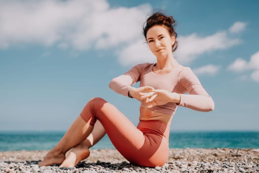 Young woman with long hair in white swimsuit and boho style braclets practicing outdoors on yoga mat by the sea on a sunset. Women's yoga fitness routine. Healthy lifestyle, harmony and meditation