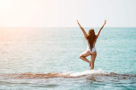 Woman sea yoga. Back view of free calm happy satisfied woman with long hair standing on top rock with yoga position against of sky by the sea. Healthy lifestyle outdoors in nature, fitness concept.