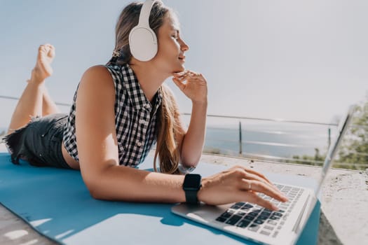 Digital nomad, Business woman working on laptop by the sea. Pretty lady typing on computer by the sea at sunset, makes a business transaction online from a distance. Freelance, remote work on vacation