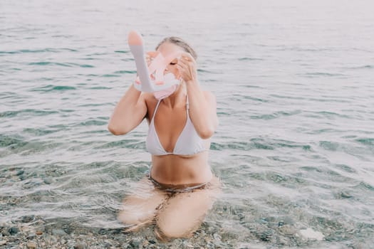 Young happy woman in white bikini put pink snorkeling mask on beach before swimming. girl having fun relaxing on beautiful beach. Beach lifestyle