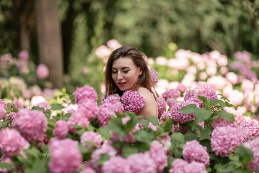 Hydrangeas Happy woman in pink dress amid hydrangeas. Large pink hydrangea caps surround woman. Sunny outdoor setting. Showcasing happy woman amid hydrangea bloom