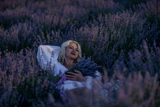 Blonde woman poses in lavender field at sunset. Happy woman in white dress holds lavender bouquet. Aromatherapy concept, lavender oil, photo session in lavender.