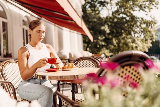 Portrait of happy woman sitting in a cafe outdoor drinking coffee. Woman while relaxing in cafe at table on street, dressed in a white T-shirt and jeans.