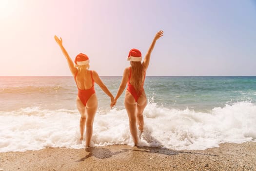 Women Santa hats ocean play. Seaside, beach daytime, enjoying beach fun. Two women in red swimsuits and Santa hats are enjoying themselves in the ocean waves and raising their hands up