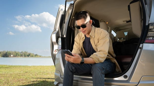 Young solo traveler man sitting on the open trunk over blue sky. Travel and active lifestyle concept.