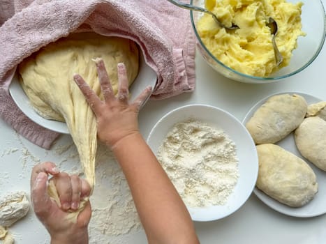 The hands of child knead the dough for making pies on white table, top view. High quality photo