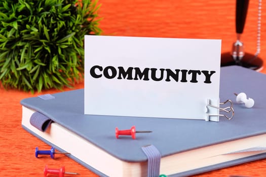The word Community written on a business card standing with a clip on a diary, a notebook on an orange background