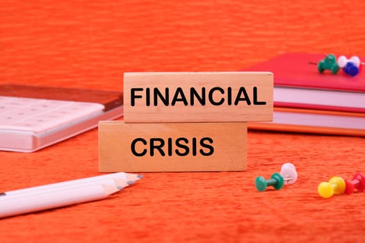 FINANCIAL CRISIS text written on a wooden block on an orange background next to office supplies