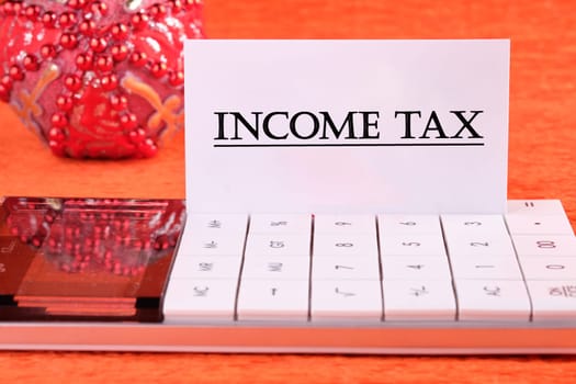 INCOME TAX text written on a white business card on a calculator on an orange background