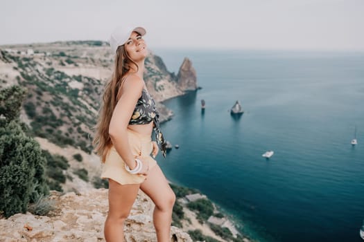 Woman travel sea. Happy tourist taking picture outdoors for memories. Woman traveler looks at the edge of the cliff on the sea bay of mountains, sharing travel adventure journey.