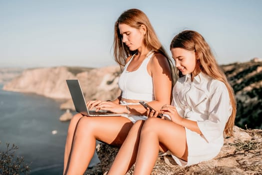 Successful business woman in yellow hat working on laptop by the sea. Pretty lady typing on computer at summer day outdoors. Freelance, travel and holidays concept.