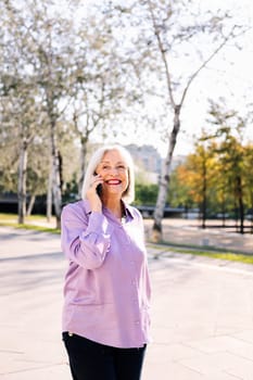 senior woman smiling happy talking by mobile phone while walking at park, concept of technology and elderly people leisure, copy space for text