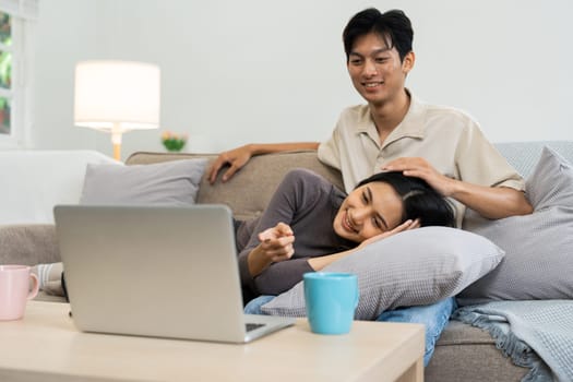 Happy young couple looking laptop relax on sofa in living room watch video on laptop together.
