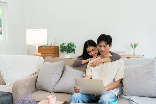 Happy young couple looking laptop relax on sofa in living room watch video on laptop together.