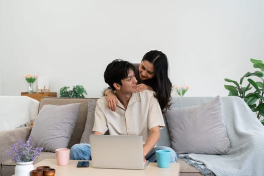 Happy young couple looking laptop relax on sofa in living room watch video on laptop together.